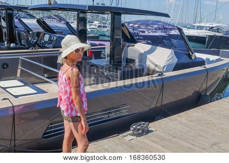 girl in hat and sunglasses walking on pier among luxury yachts