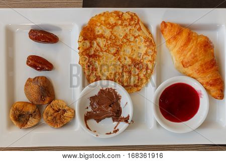 dates, figs, pancake, chocolate, sweet sauce and croissant at compartmental dish