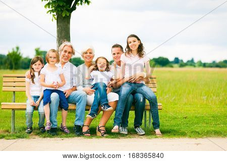 a big family are sitting on a bench in a park