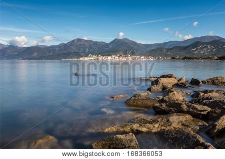 View across the bay of Saint Florent in Corsica with rocks in the foreground and the mountains of Cap Corse behind the town of Saint Florent