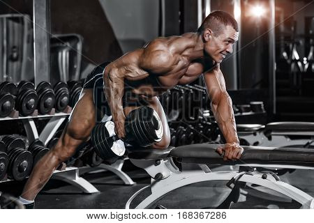 Athlete muscular bodybuilder training hands with dumbbells in gym