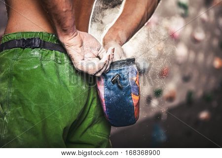 Climber man coating his hands in powder chalk magnesium and preparing to climb indoor close-up