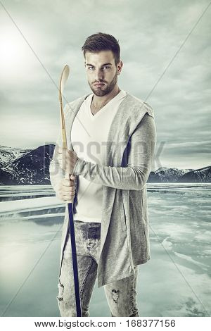 Young athlete with the caman standing on the background of iced mountain lake.
