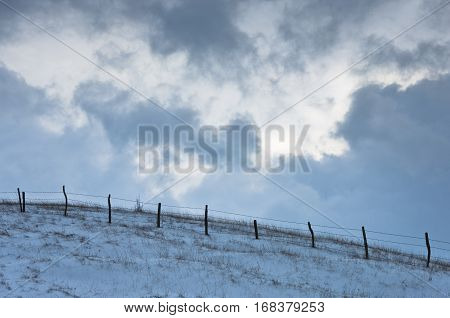Hill with a fence covered with snow under dramatic clouds at winter, mountain Kozomor, Serbia