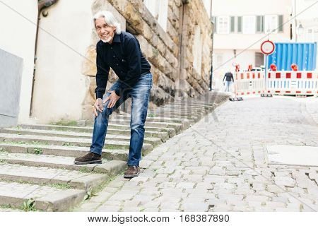 Senior walking through city, suffering from knee pain
