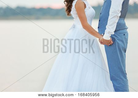 Beautiful wedding couple holding hands near river, close up view