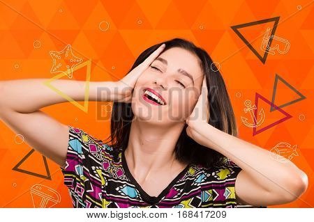 Beautiful smiling girl, with straight dark hair, wearing on colorful shirt, posing on the orange geometric background with colorful triangles and sea set anchor, starfish, dive mask icons, in studio, waist up