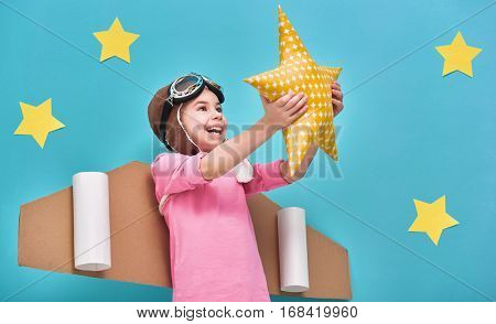 Little child girl in an astronaut costume is playing and dreaming of becoming a spaceman. Portrait of funny kid on a background of bright blue wall with yellow stars.