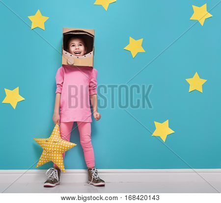 Child girl in an astronaut costume is playing and dreaming of becoming a spacemen. Portrait of funny kid on a background of bright blue wall with yellow stars.