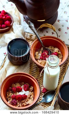Muesli with raspberries and milk. Black hot tea in mugs. Food located on a wicker tray.