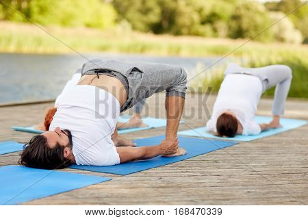fitness, sport, yoga and healthy lifestyle concept - group of people making bridge pose on river or lake berth