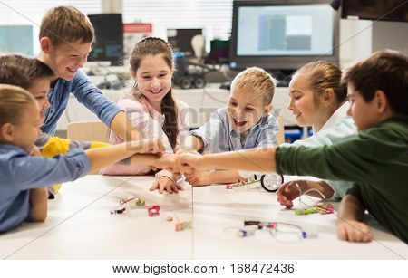 education, children, technology, science and people concept - group of happy kids building robots at robotics lesson and making fist bump