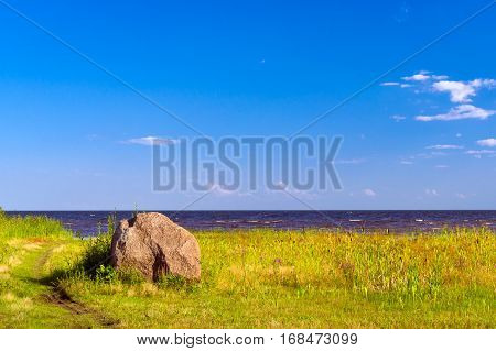Shore of lake Peipsi in Eastern Estonia. Chudskoye is large freshwater lake with rich history where occurred famous battle of Ice. Huge granite stones among grass & reeds near water. Fishing village