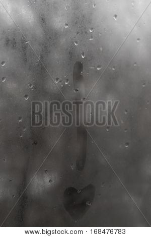 The exclamation point with a point-heart on the glass with rain drops on a gray sky background