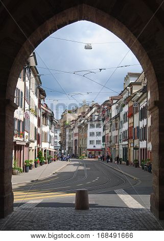 Basel, Switzerland - July 12, 2014. View of Spalenvorstadt street through the 600-year-old Spalentor city gate in Basel, with historic buildings, tram tracks, commercial properties and people.