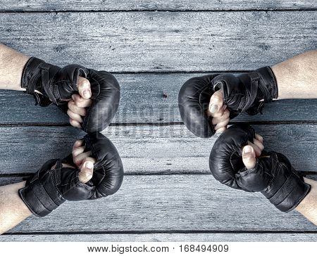 Two pairs of human hands in black leather boxing gloves facing each other a vintage wooden background