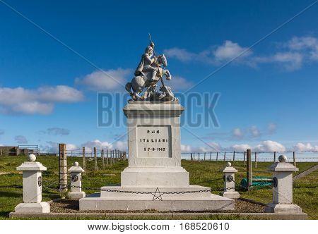 Orkneys Scotland - June 5 2012: White concrete statue of Saint George sitting on horse defeating a dragon against deep blue sky standing on a green meadow outside the Italian Chapel on Lamb Holm Island.