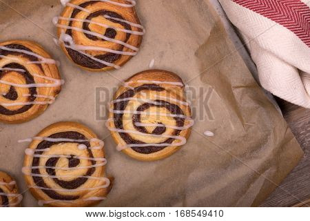 Overhead view of freshly baked cinnamon buns on greaseproof paper, with tea towel and old wood background. 