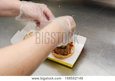 The cook prepares a burger. Fries cutlet greens lay down. Cuts a roll. Pours sauce.