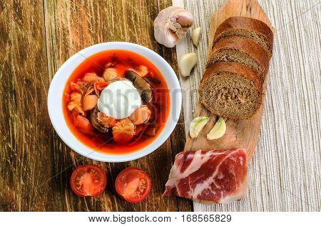 Red vegetable soup in the white plate and bread. On a wooden background.