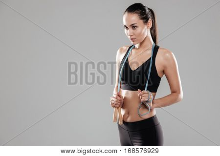 Sporting woman with skipping rope looking away. Isolated gray background
