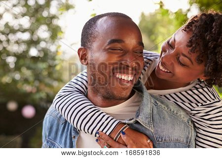 Smiling young black couple piggyback in garden, eyes closed