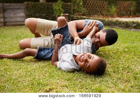 Black father and young son play lying on grass, low angle
