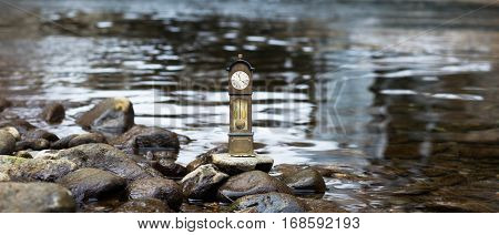 Model standing clock stands on a pebble by the waterside