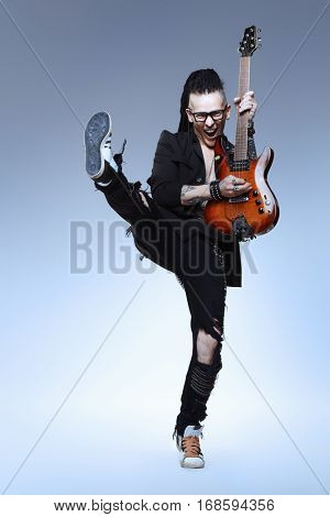 Entertainment and musical concept. Excited rock musician is jumping with his electrical guitar. Full length studio shot. 