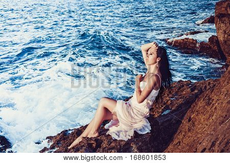 Girl with bare feet sitting on the rocks by the sea