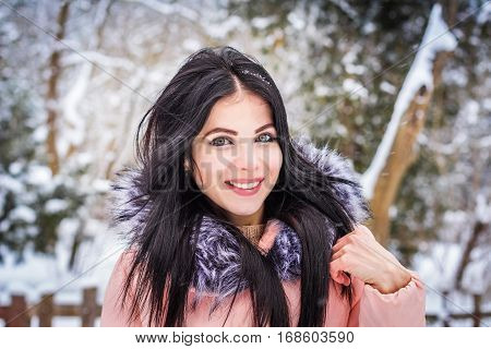 Winter. Girl brunette capless smiles on the background of snow. Close-up