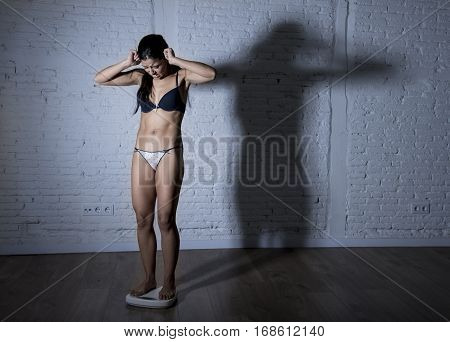 young fit and slim woman or teenager girl checking body weight on scale with big edgy shadow light sad desperate and frustrated in anorexia and bulimia nutrition disorder and overweigh obsession
