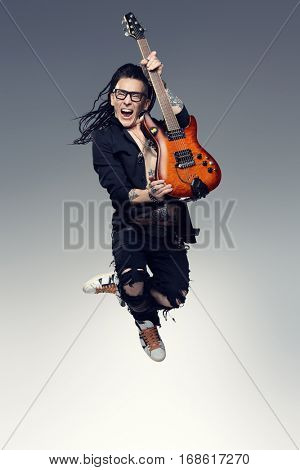 Entertainment and musical concept. Excited rock musician is jumping with his electrical guitar. Full length studio shot. 