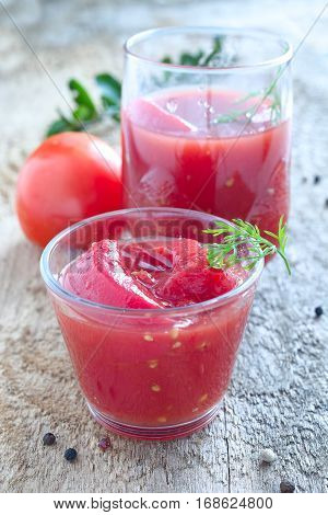 Whole canned red tomatoes in a glass and red tomato.