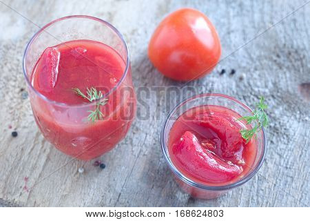 Whole canned red tomatoes in a glass and red tomato.