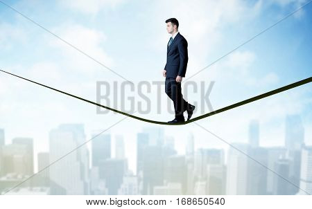City scape, tall buildings and clouds on clear blue sky with business person balancing on black rope concept