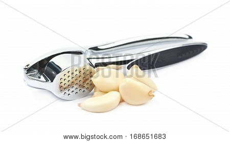 Metal garlic press utensil next to a pile of fresh cloves isolated over the white background