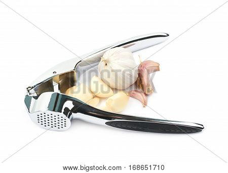 Metal garlic press utensil next to a pile of fresh cloves isolated over the white background