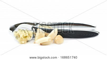 Metal garlic press utensil next to a pile of fresh cloves isolated over the white background