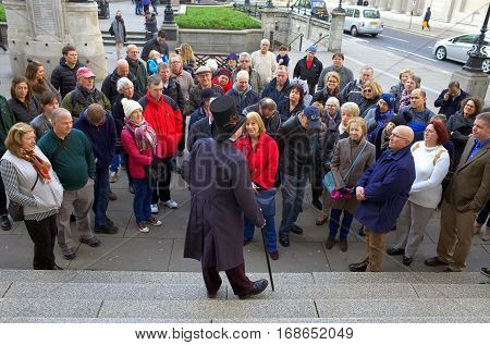 London, England - December 28, 2015: A man in a top hat and coat addresses a crowd of people as part of guided tour in Threadneedle Street, London