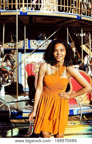 cool real modern teenage girl with candy near carousels at amusement park walking, having fun