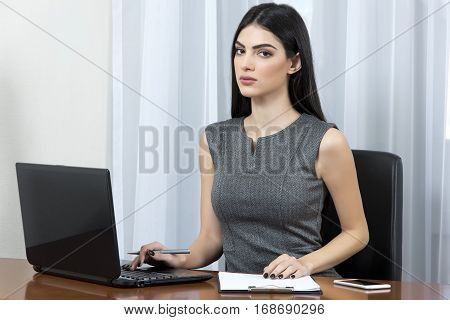 Young business woman at her office using laptop and looking at the camera.