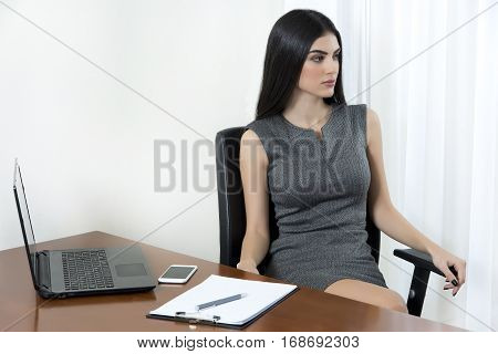 Business woman sitting at her office and looking away.