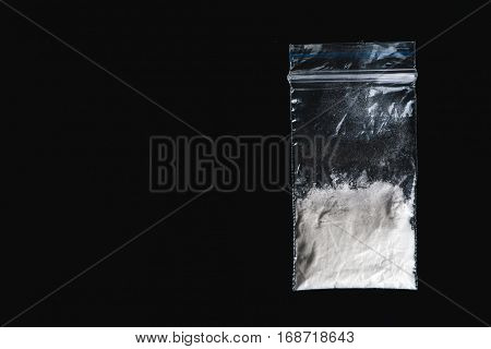 Cocaine in plastic packet on black background, closeup. Portion of drugs. Top view with copy space