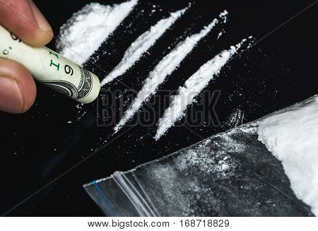 Hand of man holds rolled banknote for snorting line of cocaine powder. Problems with drugs concept