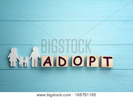 Cubes with word ADOPT and figure in shape of happy family on wooden background
