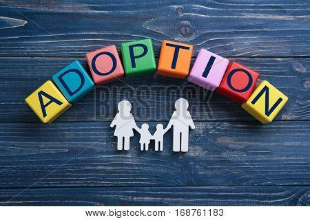 Cubes with word ADOPTION and figure in shape of family on wooden background