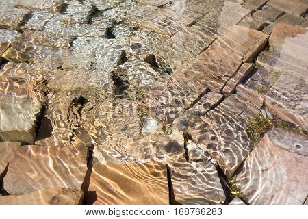 Cobblestone underneath of shallow water pool with reflective sunspots and light circles