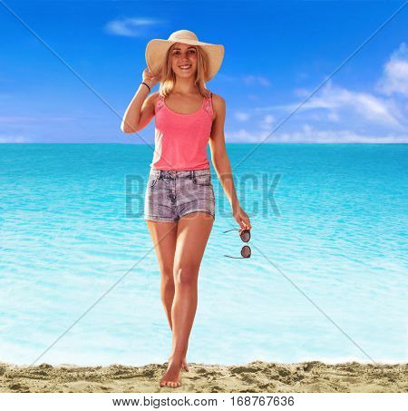 Young blonde woman walking on the beach wearing sun glasses and hat.