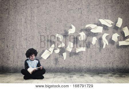 Young guy reading a book with flying sheets coming out of the book